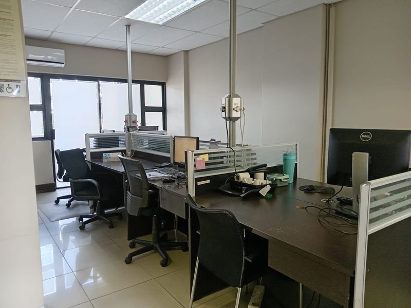 A functional office space featuring tiled flooring, suspended ceiling, and integrated electrical power poles, suitable for a professional work environment.