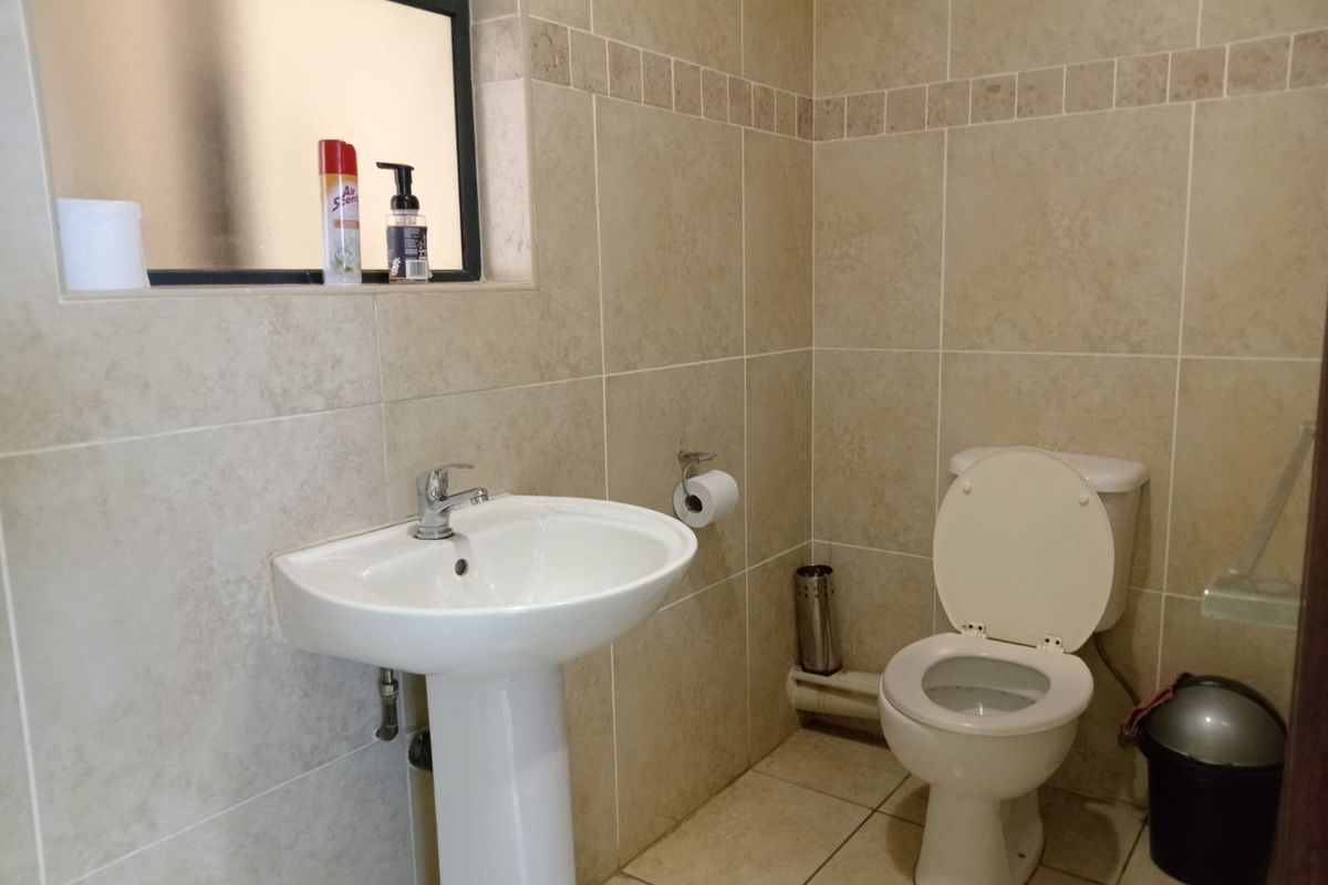 A functional bathroom featuring a pedestal basin, chrome mixer tap, ceramic toilet, and neutral wall and floor tiling with a frosted glass window.