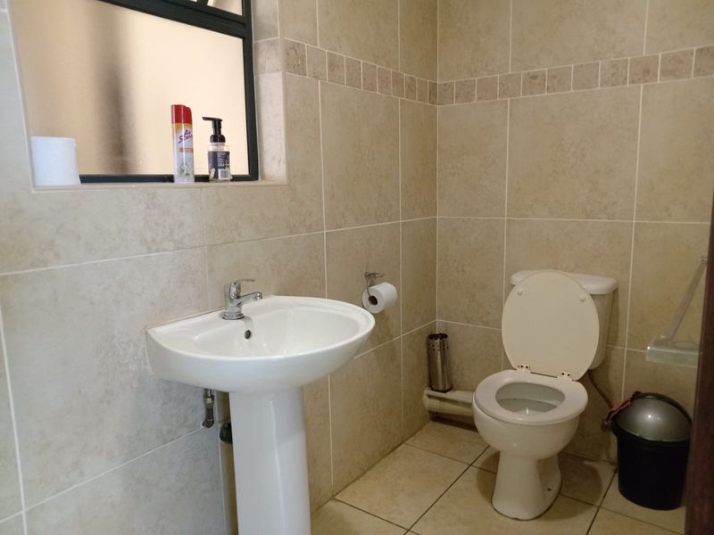 A functional bathroom featuring a pedestal basin, chrome mixer tap, ceramic toilet, and neutral wall and floor tiling with a frosted glass window.