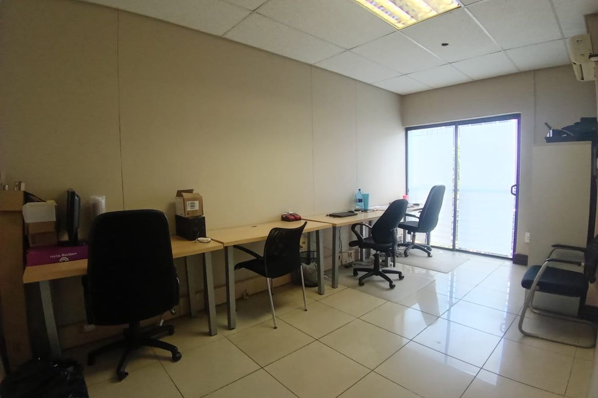 A functional office space featuring tiled flooring, a drop ceiling with integrated lighting, and a sliding glass door providing natural light.