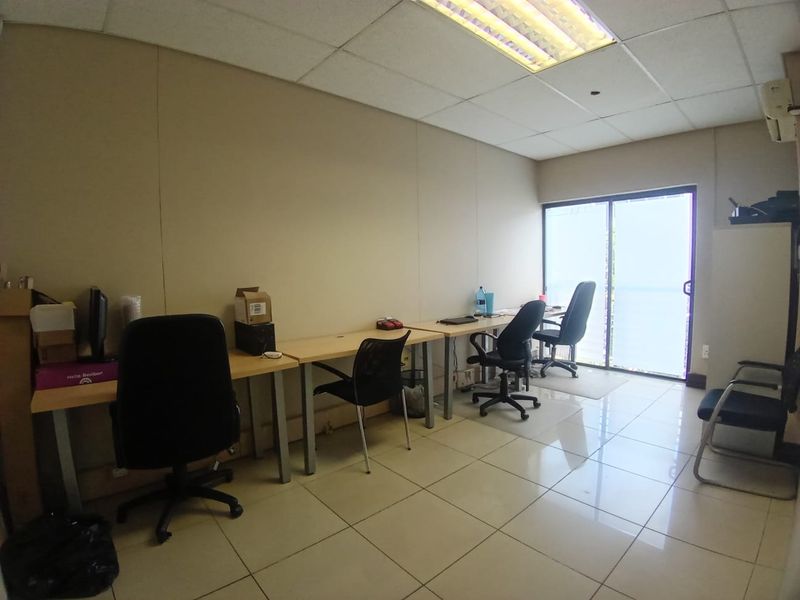 A functional office space featuring tiled flooring, a drop ceiling with integrated lighting, and a sliding glass door providing natural light.
