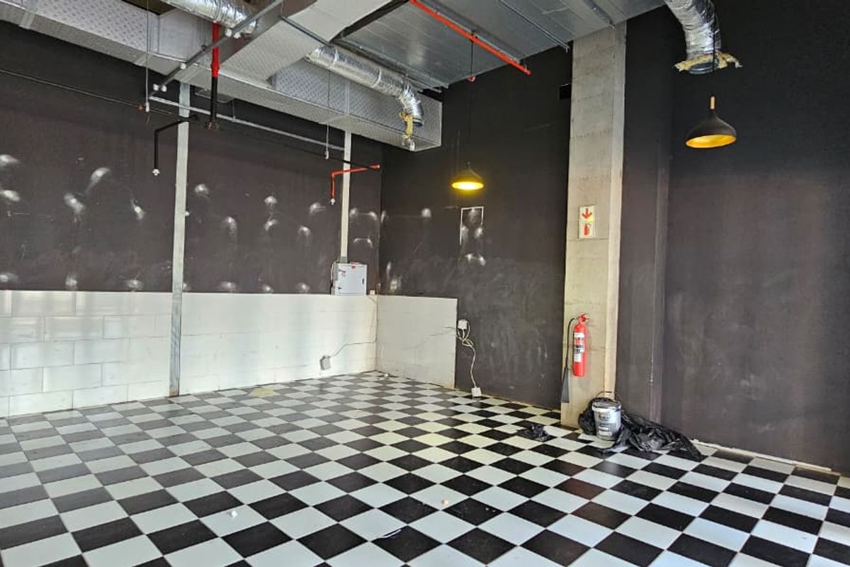 An empty open-plan retail space featuring industrial exposed ducting, checkered tile flooring, and fire safety infrastructure, ready for custom fit-out.