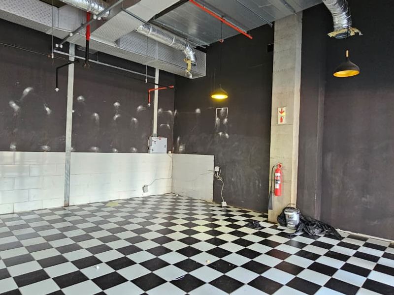An empty open-plan retail space featuring industrial exposed ducting, checkered tile flooring, and fire safety infrastructure, ready for custom fit-out.