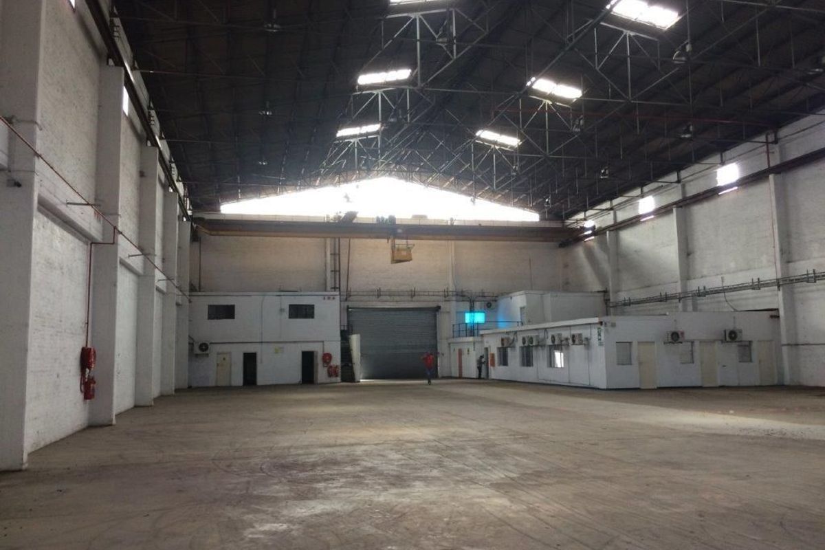 Spacious industrial warehouse featuring high ceilings with exposed steel trusses, overhead crane, concrete flooring, and integrated internal office structures.