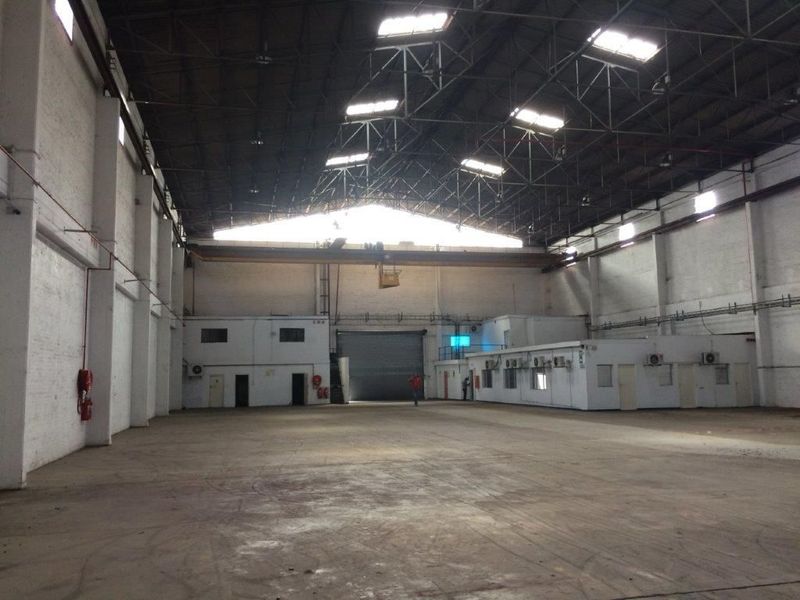 Spacious industrial warehouse featuring high ceilings with exposed steel trusses, overhead crane, concrete flooring, and integrated internal office structures.