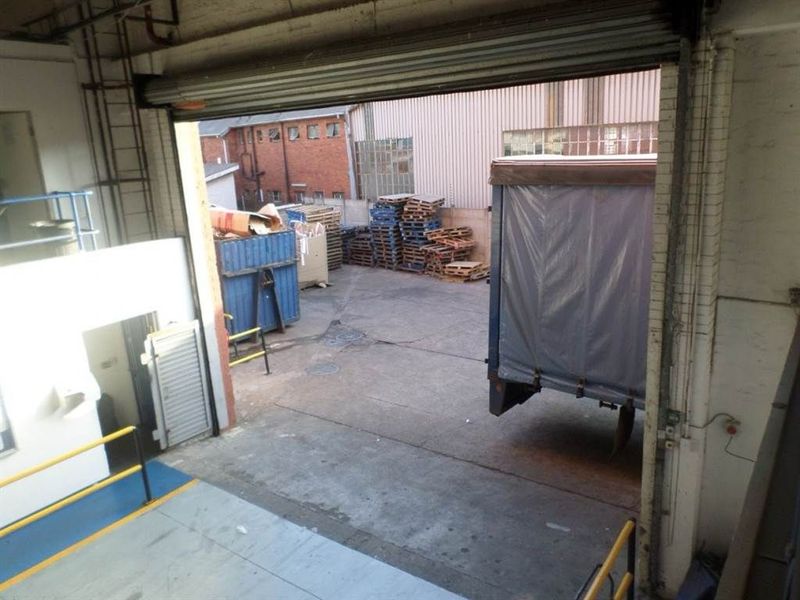 Industrial loading bay area featuring a large roller shutter door, concrete flooring, and safety railings, providing direct access to the exterior yard.