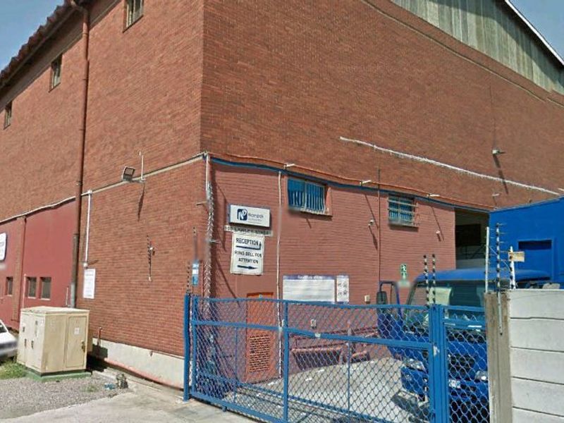 Industrial property exterior featuring a brick facade, secure gated entrance, and perimeter security fencing.