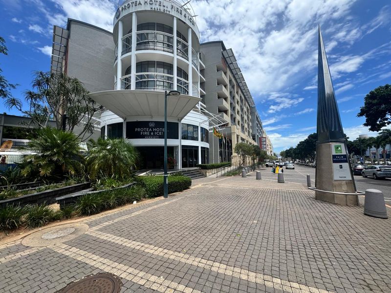 A clear street-level view of the modern hotel facade, featuring a prominent entrance canopy, paved pedestrian area, and professional landscaping.