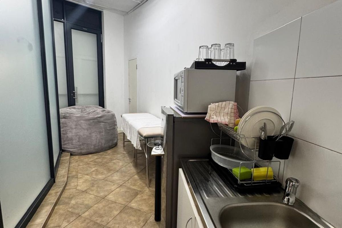 A compact kitchenette area featuring a stainless steel sink, tiled splashback, and tiled flooring, suitable for office utility or breakroom use.