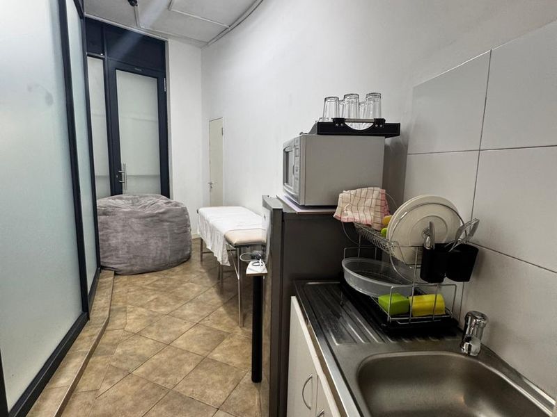 A compact kitchenette area featuring a stainless steel sink, tiled splashback, and tiled flooring, suitable for office utility or breakroom use.