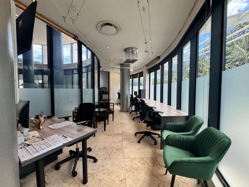 Modern office space featuring extensive floor-to-ceiling windows, tiled flooring, and a bright, open layout suitable for a professional work environment.