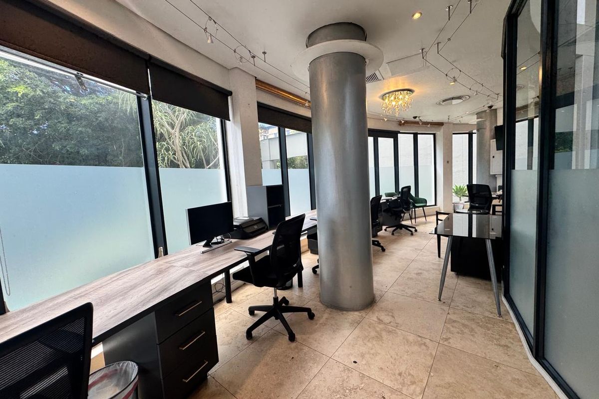 Modern open-plan office space featuring large windows, structural columns, tiled flooring, and glass partitions, offering a bright and professional work environment.