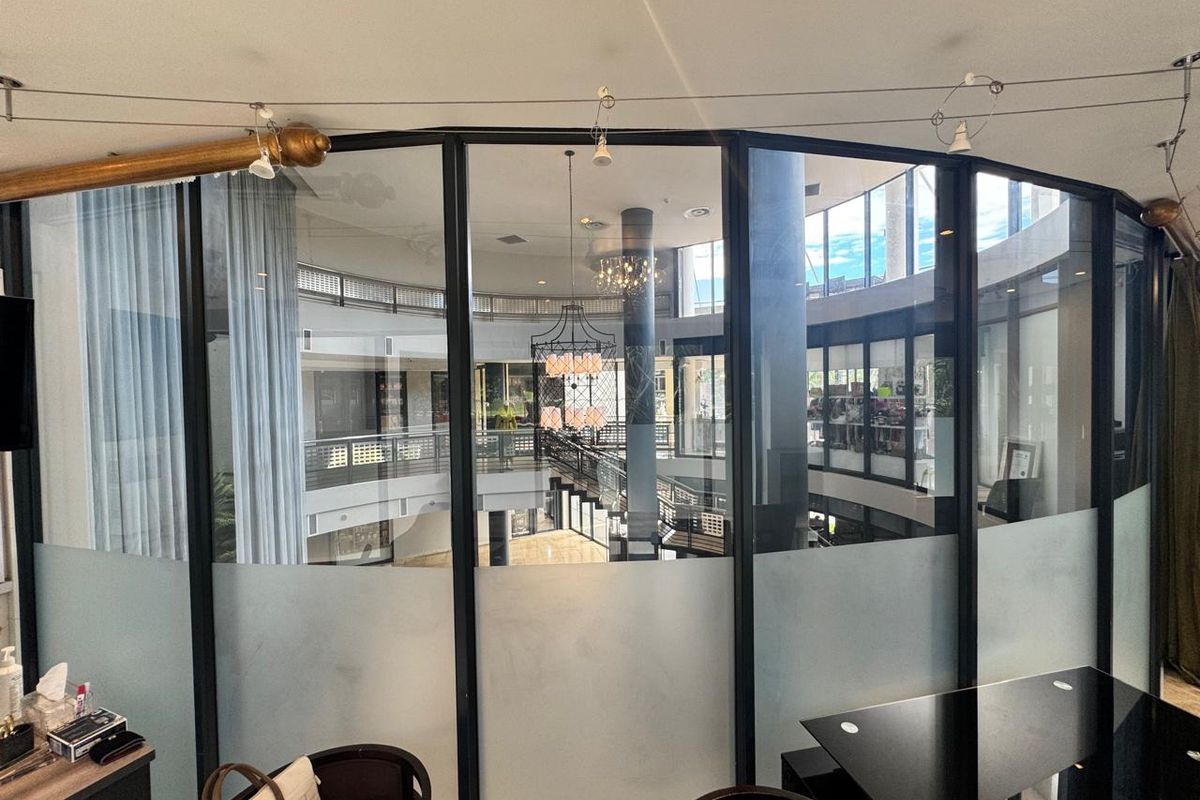 Modern office space featuring a curved frosted glass partition with black metal framing, overlooking a central atrium area.