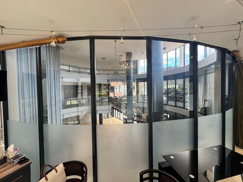 Modern office space featuring a curved frosted glass partition with black metal framing, overlooking a central atrium area.