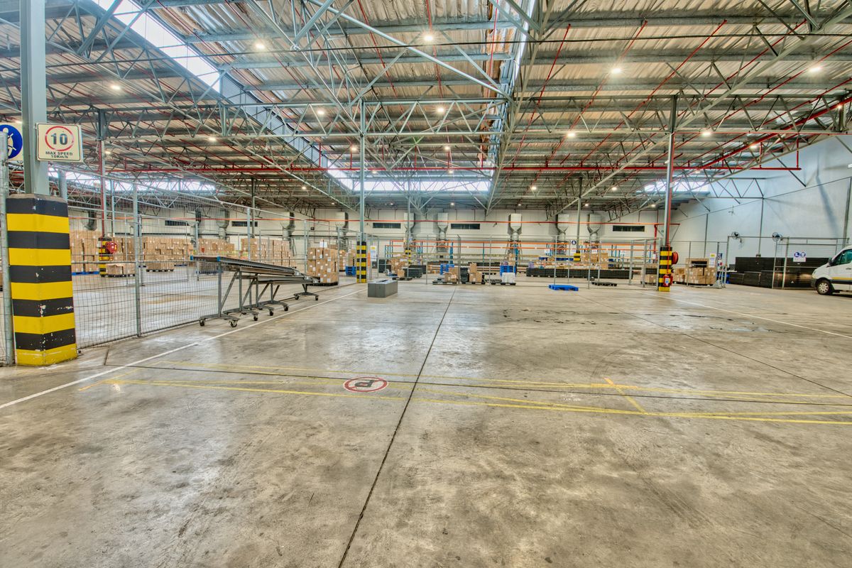 Spacious industrial warehouse featuring high-clearance steel truss roofing, polished concrete flooring, and integrated fire safety systems, suitable for logistics or manufacturing operations.