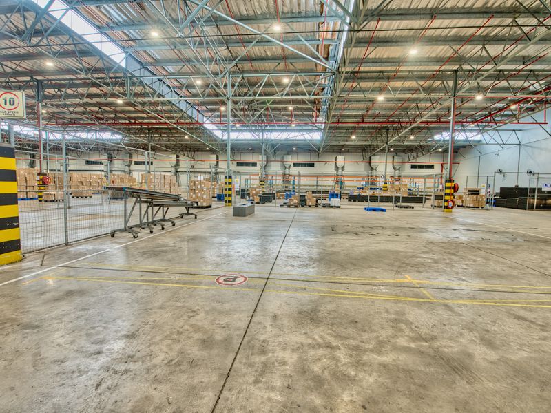Spacious industrial warehouse featuring high-clearance steel truss roofing, polished concrete flooring, and integrated fire safety systems, suitable for logistics or manufacturing operations.