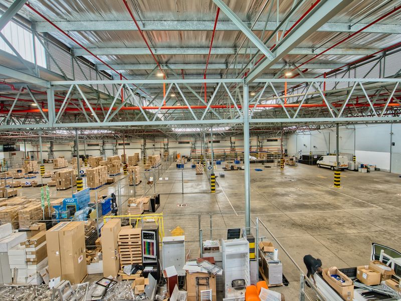 Spacious industrial warehouse featuring high-clearance exposed steel truss roofing, fire sprinkler systems, and durable concrete flooring with wire mesh partitioning.