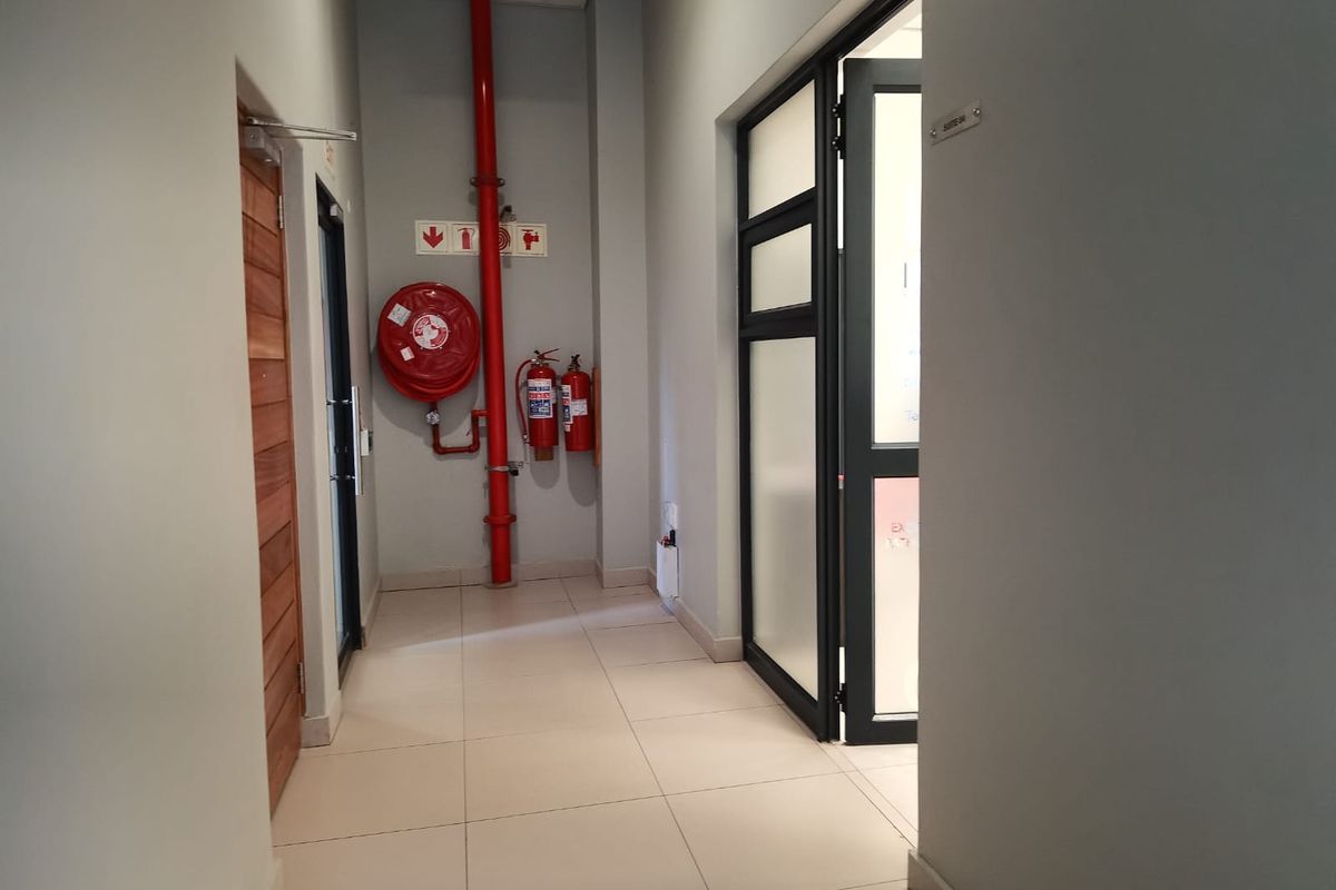 A clean commercial hallway featuring tiled flooring, fire safety equipment including a hose reel and extinguishers, and access to office suites.