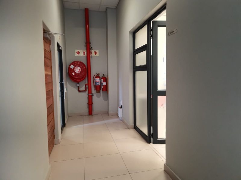 A clean commercial hallway featuring tiled flooring, fire safety equipment including a hose reel and extinguishers, and access to office suites.
