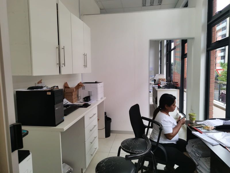 A functional office space featuring built-in white cabinetry, tiled flooring, and large windows providing natural light and views of the exterior.