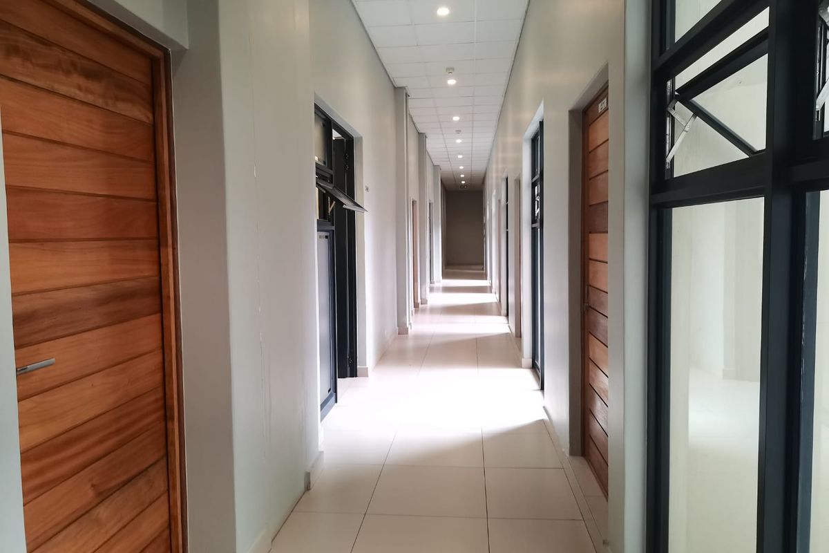 A clean, modern commercial hallway featuring tiled flooring, recessed downlights, and multiple timber doors leading to individual office or utility spaces.