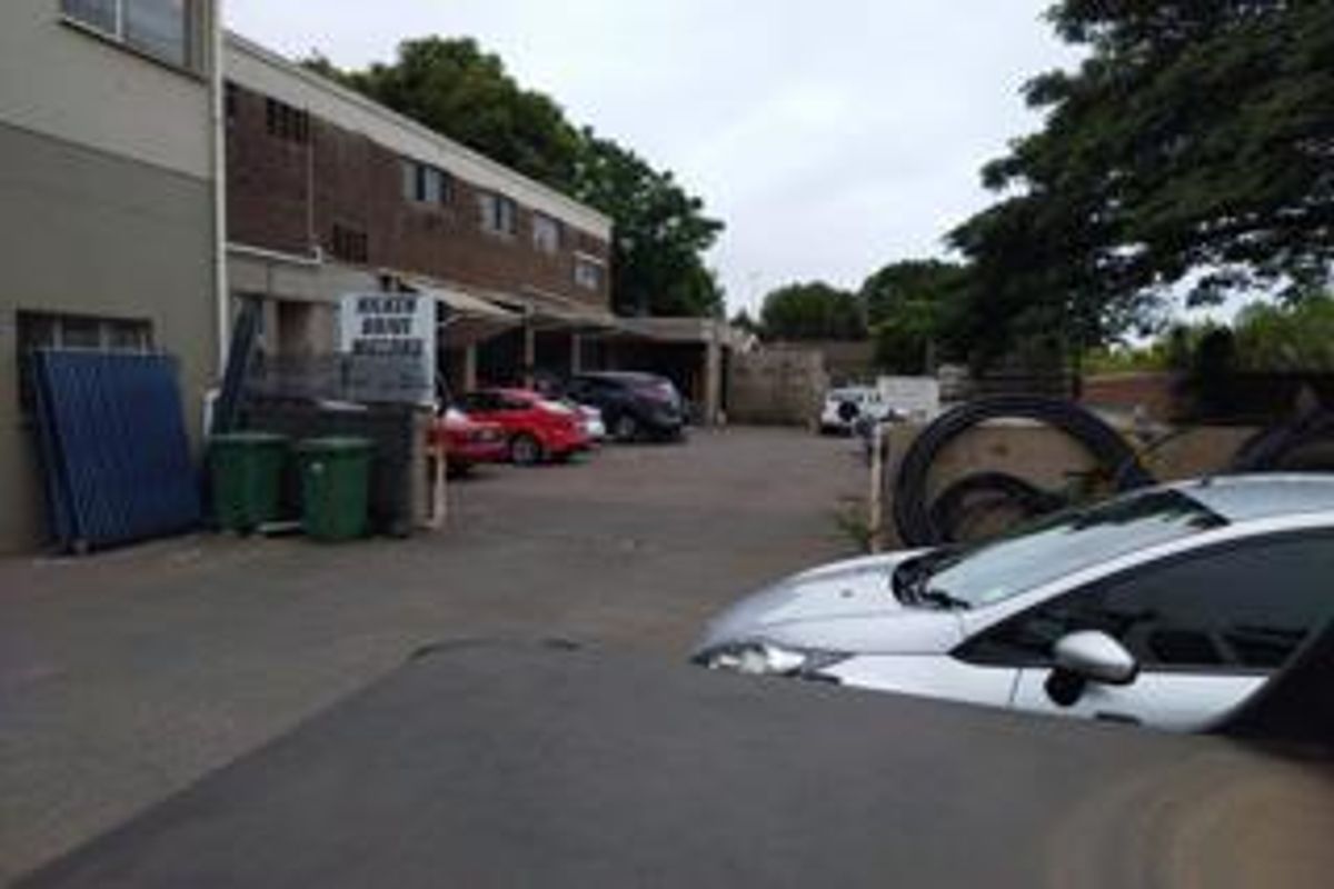 Rear exterior view of a commercial property featuring a paved parking area and brick building facade.