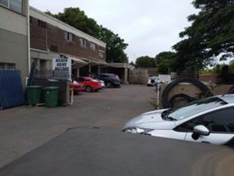 Rear exterior view of a commercial property featuring a paved parking area and brick building facade.