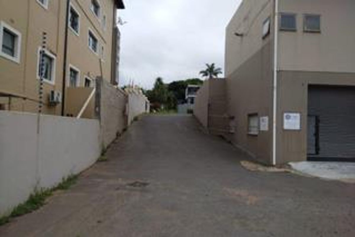 Rear access driveway featuring asphalt paving, perimeter walling with electric fencing, and a secure roller shutter door entrance.