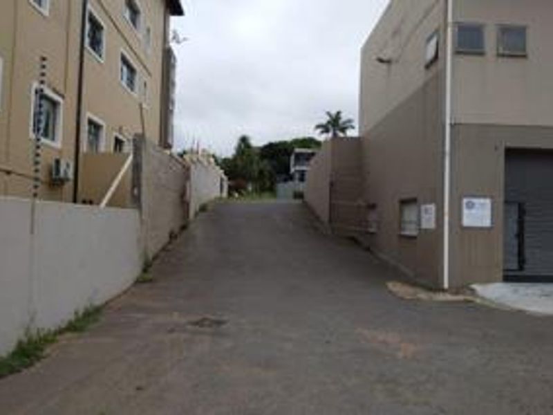 Rear access driveway featuring asphalt paving, perimeter walling with electric fencing, and a secure roller shutter door entrance.