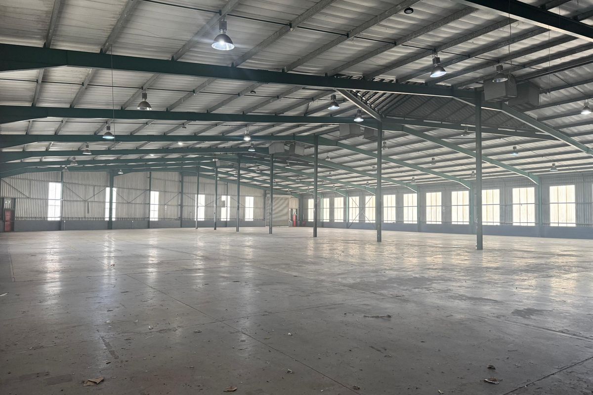 Expansive industrial warehouse space featuring a high-clearance steel portal frame, concrete flooring, and abundant natural light through large perimeter windows.
