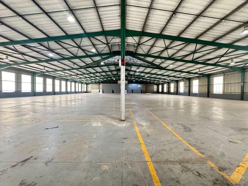 Expansive industrial warehouse space featuring a high-clearance steel portal frame, concrete flooring, and ample natural light through perimeter windows.