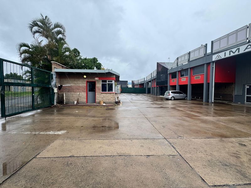 Industrial property entrance featuring a guard house, concrete paved yard, and multi-unit industrial building facade with secure perimeter fencing.