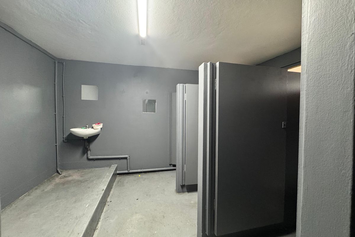 Industrial-style communal bathroom featuring multiple toilet cubicles, a wall-mounted basin, and exposed plumbing fixtures.