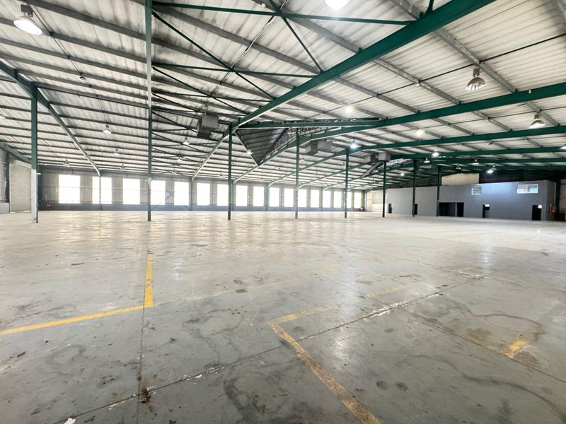 Large, open-plan industrial warehouse space featuring high exposed steel truss ceilings, polished concrete flooring, and ample natural light through side windows.