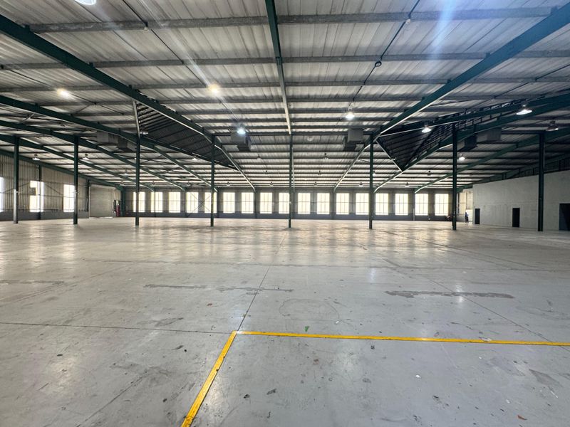 Spacious industrial warehouse featuring high ceilings with exposed steel trusses, polished concrete flooring, and ample natural light through perimeter windows.