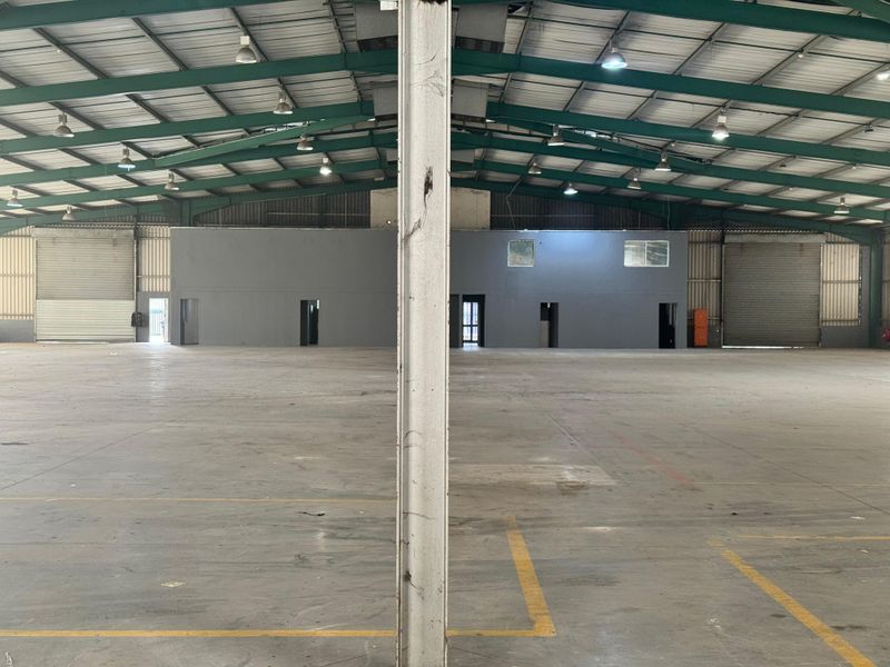 Spacious industrial warehouse featuring high ceilings, concrete flooring, multiple roller shutter doors, and an internal office partition wall.