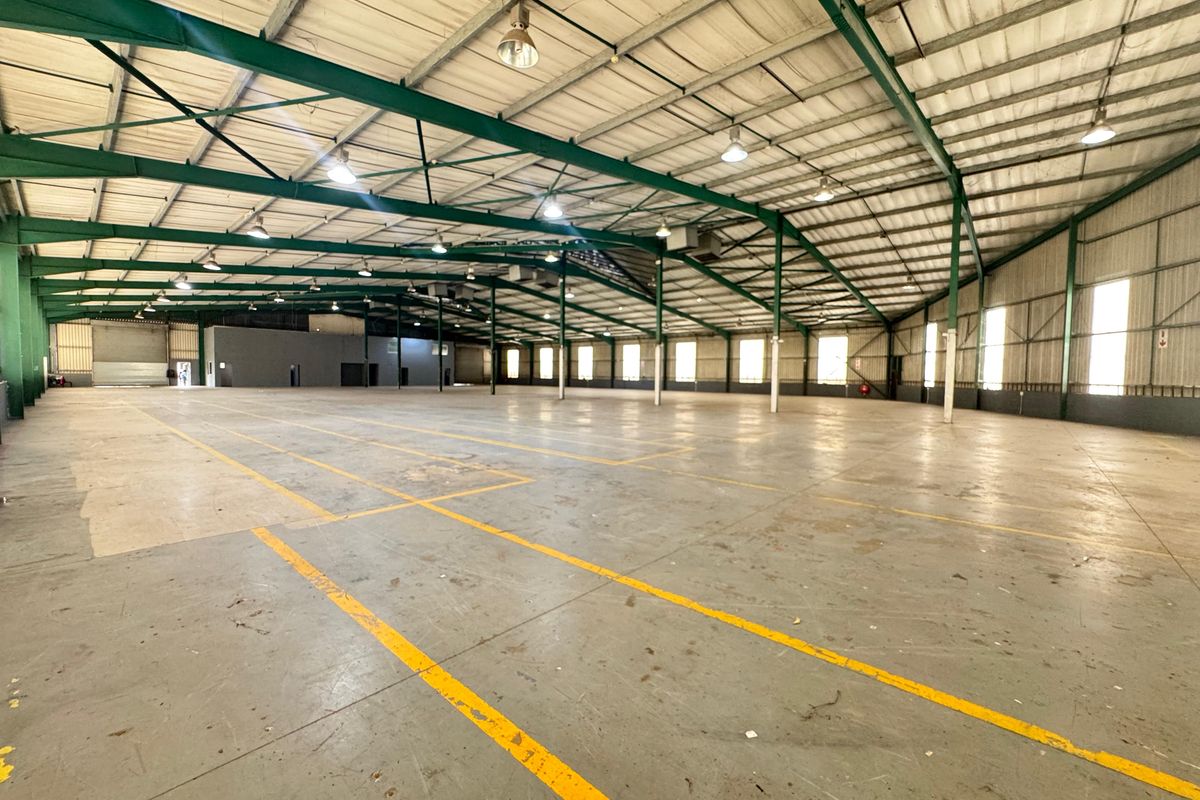 Expansive industrial warehouse space featuring a high-clearance steel portal frame, concrete flooring, and abundant natural light through side windows.