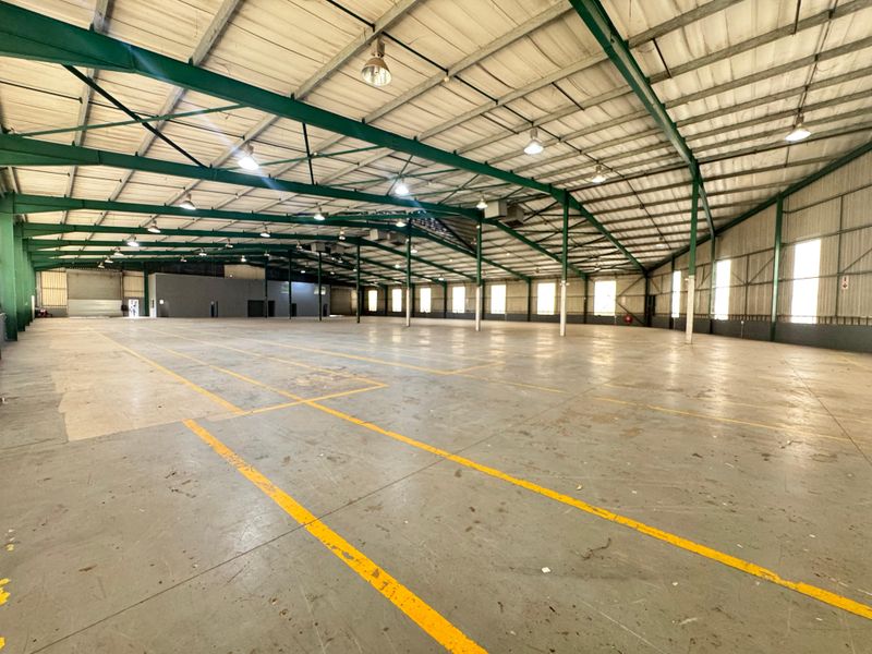 Expansive industrial warehouse space featuring a high-clearance steel portal frame, concrete flooring, and abundant natural light through side windows.