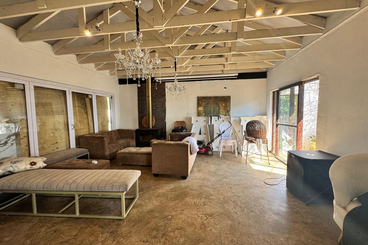 Spacious living area featuring exposed timber roof trusses, a central fireplace with brick surround, polished concrete floors, and extensive natural light from large sliding doors.