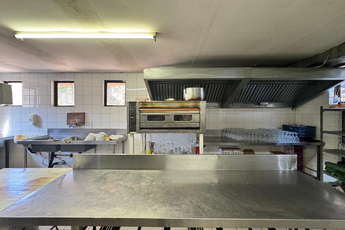 Commercial kitchen space featuring stainless steel prep surfaces, a built-in oven, commercial extractor hood, and tiled wall finishes.