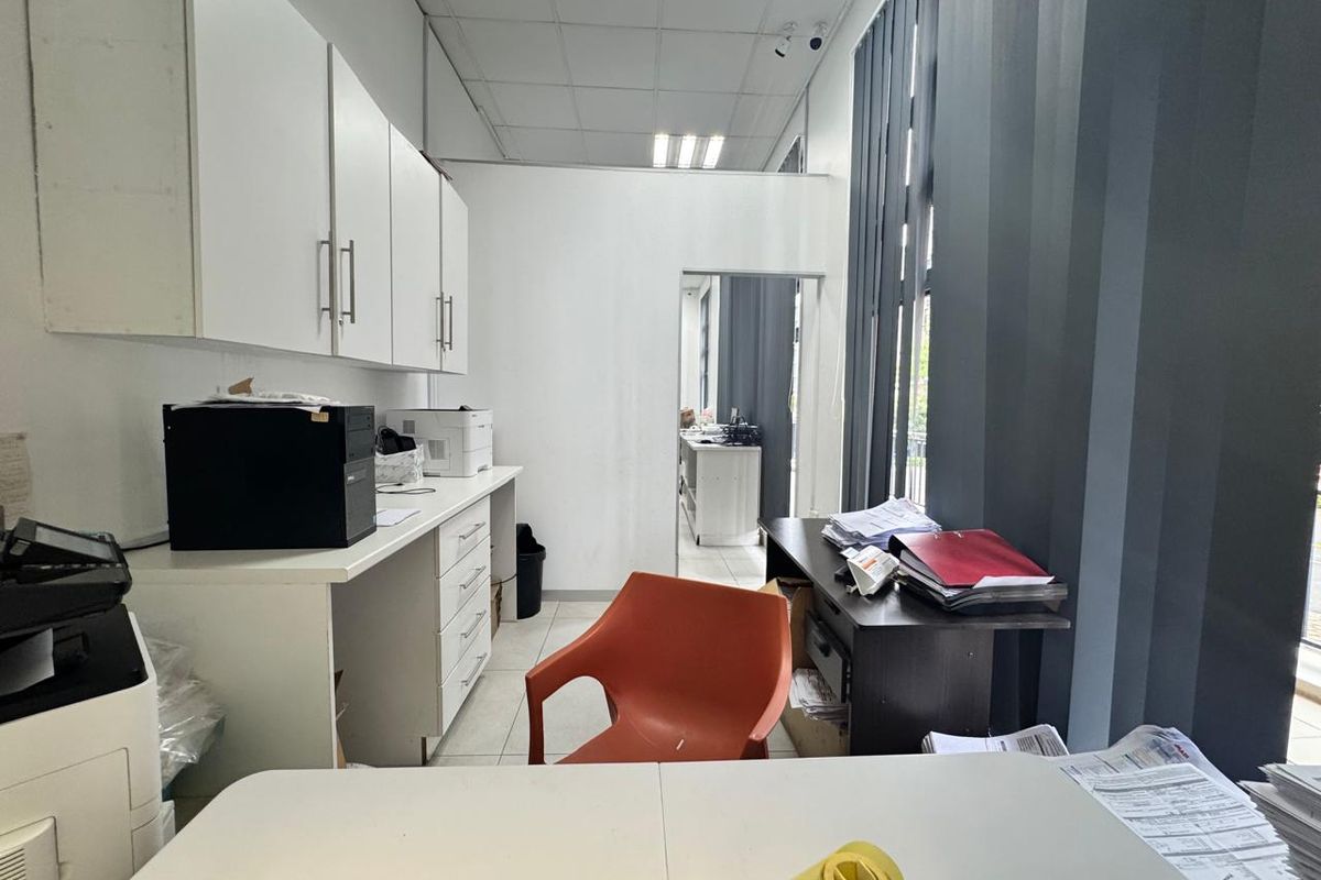 Functional office space featuring built-in cabinetry, drop ceiling, and large windows with vertical blinds, providing a practical workspace environment.