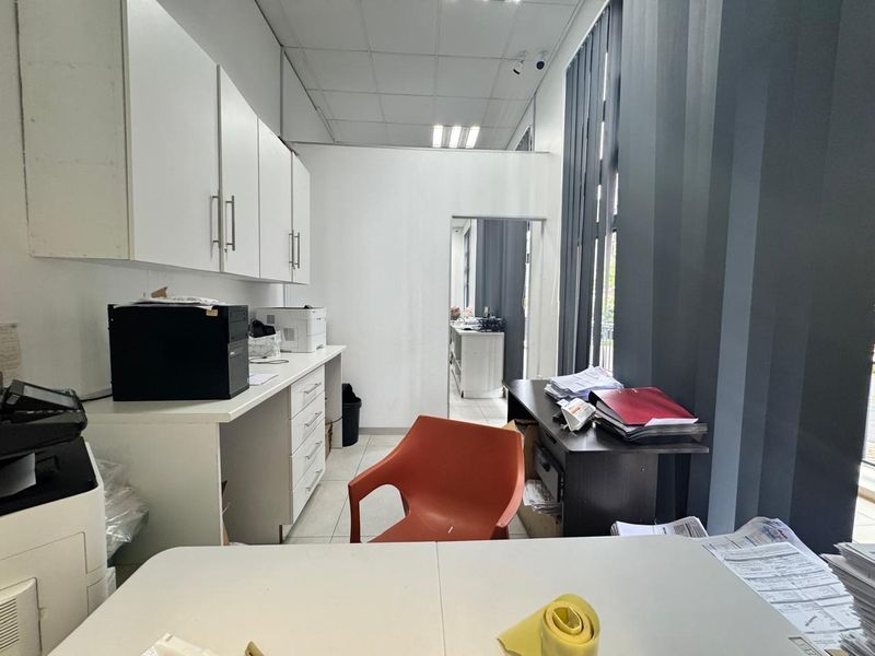 Functional office space featuring built-in cabinetry, drop ceiling, and large windows with vertical blinds, providing a practical workspace environment.
