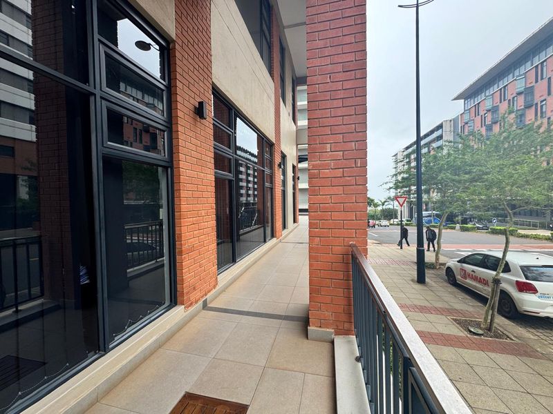 A commercial building exterior featuring a brick facade, large glass windows, and a paved walkway overlooking the street.