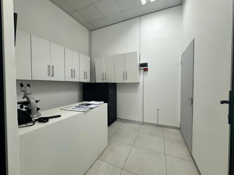 A clean, functional utility or laboratory space featuring ample built-in white cabinetry, tiled flooring, and a suspended ceiling.