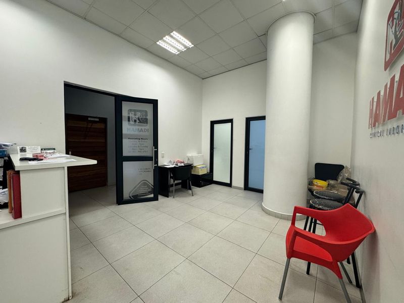 A commercial reception area featuring tiled flooring, a structural column, and glass-paneled entry doors with a suspended ceiling.