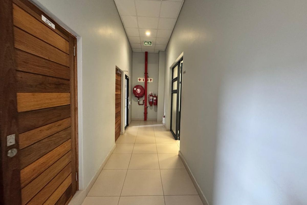 A clean, well-maintained commercial hallway featuring tiled flooring, suspended ceiling, and integrated fire safety equipment including a hose reel and extinguishers.