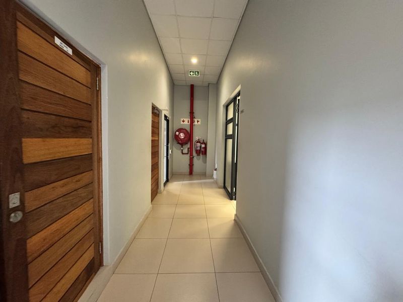 A clean, well-maintained commercial hallway featuring tiled flooring, suspended ceiling, and integrated fire safety equipment including a hose reel and extinguishers.