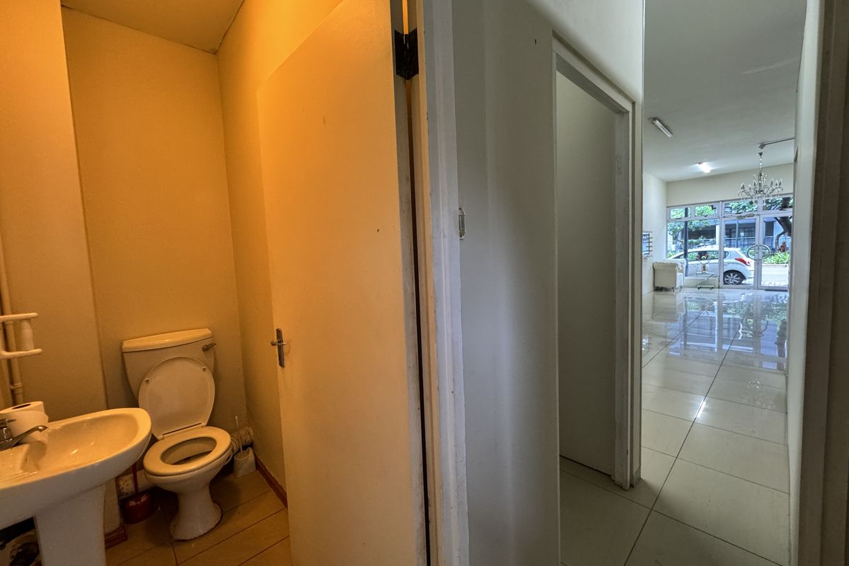 A small, functional bathroom featuring a pedestal sink and toilet, with direct access to the main retail floor area.