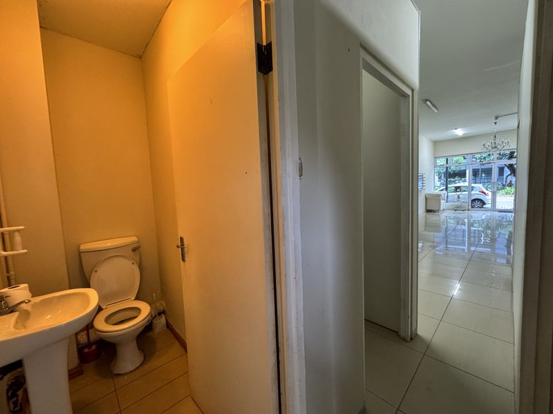 A small, functional bathroom featuring a pedestal sink and toilet, with direct access to the main retail floor area.