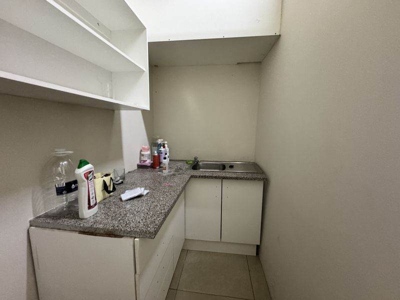 A compact scullery or utility area featuring built-in cabinetry, a granite countertop, and a stainless steel sink with overhead shelving.